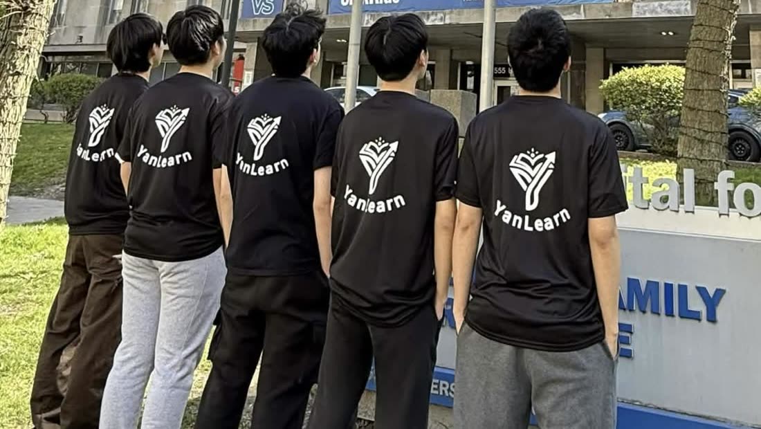 Five members of the YanLearn team in branded shirts, seen from behind, in front of the Hospital for Sick Children.